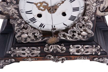 Europe, 18th century, bracket or shelf clock with cow tail pendulum, ebonized wooden case with applied moldings and laden with leaf and scroll, repousse silver ornaments, and case sides with applied scroll ornaments Roman numeral white enamel dial with raised chapter and concave center, fancy pierced and engraved brass hands, brass time and strike movement probably of two day duration, with verge escapement, and engraved, star shaped pendulum swinging in front of the dial