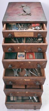 Assorted clock and watch tools in six drawer wood cabinet. Tools include a small bench vise, alcohol torches, truing calipers, pliers, tongs, files, hammers, screw plates, pin vises, screwdrivers, tweezers, 10 WW lathe collets, and other useful hand tools.