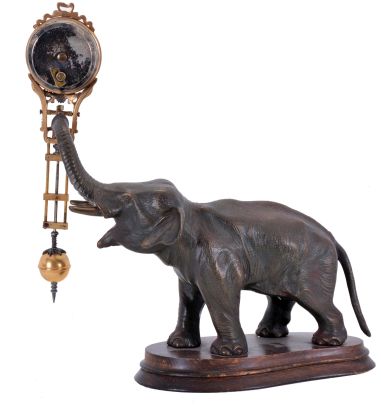 Junghans, Germany, elephant model swinging clock, patinated figure of an elephant mounted to a molded beechwood base, the 8 day swinging timepiece held aloft at the end of his trunk, clock case with gilt and silvered surfaces, Arabic numeral white enamel dial, blued steel hands, 8 day time only movement