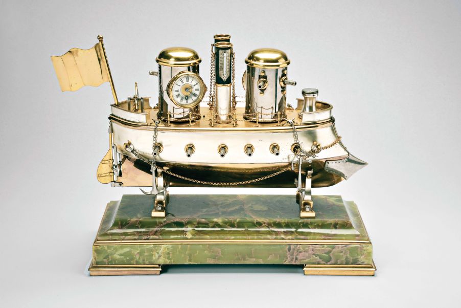 France, possibly Andre Romain Guilmet, a rare silvered and gilt brass, automated, battleship form compendium, the vessel bow with ram, fourteen cannon, and four anchors, the gilt deck with capstan containing a compass, two revolving gun turrets, one having an 11 jewel lever timepiece, with roman numeral silvered dial and blued steel trefoil hands, the other with aneroid barometer, also with silvered dial, the stacks with mounted Fahrenheit and Centigrade thermometers, the stern with ships wheel and flag, above the articulated rudder and revolving propeller, a movement concealed in the ship