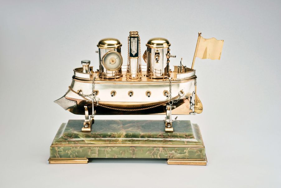 France, possibly Andre Romain Guilmet, a rare silvered and gilt brass, automated, battleship form compendium, the vessel bow with ram, fourteen cannon, and four anchors, the gilt deck with capstan containing a compass, two revolving gun turrets, one having an 11 jewel lever timepiece, with roman numeral silvered dial and blued steel trefoil hands, the other with aneroid barometer, also with silvered dial, the stacks with mounted Fahrenheit and Centigrade thermometers, the stern with ships wheel and flag, above the articulated rudder and revolving propeller, a movement concealed in the ship