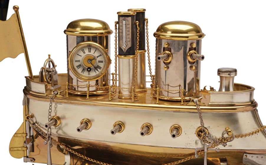 France, possibly Andre Romain Guilmet, a rare silvered and gilt brass, automated, battleship form compendium, the vessel bow with ram, fourteen cannon, and four anchors, the gilt deck with capstan containing a compass, two revolving gun turrets, one having an 11 jewel lever timepiece, with roman numeral silvered dial and blued steel trefoil hands, the other with aneroid barometer, also with silvered dial, the stacks with mounted Fahrenheit and Centigrade thermometers, the stern with ships wheel and flag, above the articulated rudder and revolving propeller, a movement concealed in the ship