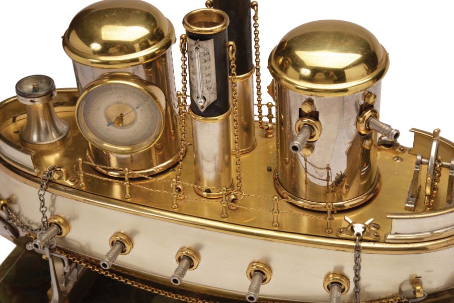 France, possibly Andre Romain Guilmet, a rare silvered and gilt brass, automated, battleship form compendium, the vessel bow with ram, fourteen cannon, and four anchors, the gilt deck with capstan containing a compass, two revolving gun turrets, one having an 11 jewel lever timepiece, with roman numeral silvered dial and blued steel trefoil hands, the other with aneroid barometer, also with silvered dial, the stacks with mounted Fahrenheit and Centigrade thermometers, the stern with ships wheel and flag, above the articulated rudder and revolving propeller, a movement concealed in the ship