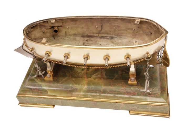 France, possibly Andre Romain Guilmet, a rare silvered and gilt brass, automated, battleship form compendium, the vessel bow with ram, fourteen cannon, and four anchors, the gilt deck with capstan containing a compass, two revolving gun turrets, one having an 11 jewel lever timepiece, with roman numeral silvered dial and blued steel trefoil hands, the other with aneroid barometer, also with silvered dial, the stacks with mounted Fahrenheit and Centigrade thermometers, the stern with ships wheel and flag, above the articulated rudder and revolving propeller, a movement concealed in the ship