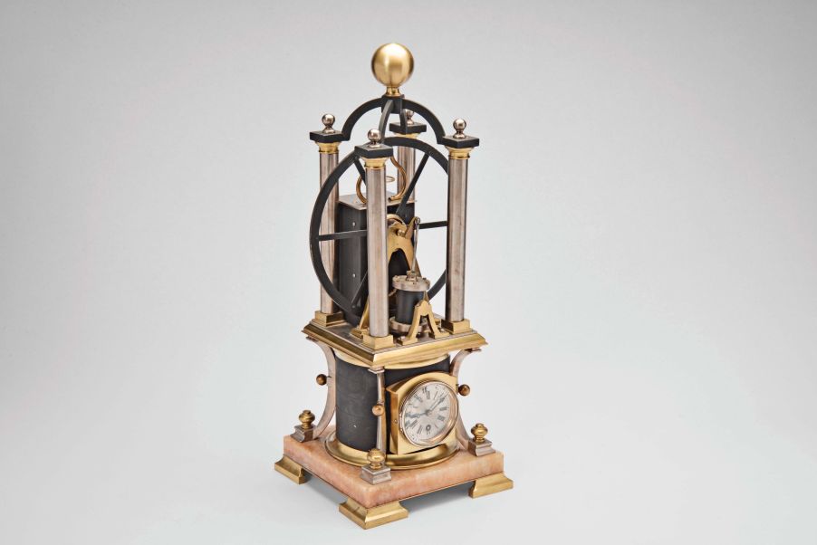 France, possibly Andre Romain Guilmet, a rare, automated, oscillating cylinder steam engine timepiece, the honey onyx square base on gilt feet, and supporting the black bronze boiler with cove molded top and bottom, below the engine itself, comprised of a large, A frame supported, spoked flywheel, connected to a rocking cylinder through a cranked linkage, the movement powering the automation contained in a black enclosure behind the engine, the enclosure top with a rotating governor in a bell shaped frame behind the wheel, surrounded by four silvered columns, and surmounted by an X shaped, arched frame with central spherical finial, the 11 jewel lever platform movement with Roman numeral silvered dial and blued steel Breguet style hands