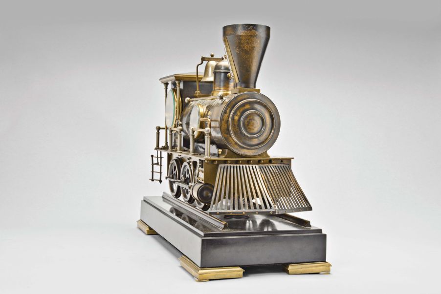 France, a rare, automated, patinated bronze locomotive form compendium, the stepped, black slate base on gilt feet with patinated rails below the large, steam locomotive, the darker surfaces highlighting the nickel, brass, and copper appointments, the engine front with cow catcher, the boiler with aneroid barometer, bell, steam dome with valve and flared stack with centigrade thermometer, the cab with shallow pitched roof, slender columns at the corners, and containing the clock and dial, a concealed movement in the base providing power to drive the six wheels, connecting rods, and piston, roman numeral brass dial, blued steel Breguet style hands, and 8 day, two train pendule de Paris movement