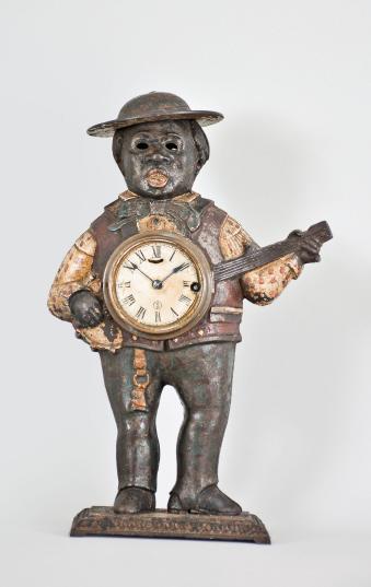 Waterbury Clock Co., "Sambo" blinking eye novelty clock, 30 hour, spring driven balance wheel movement with linkage to animate eyes in a painted cast iron case depicting a man with a banjo, roman numeral paper dial with blackened steel spade hands.