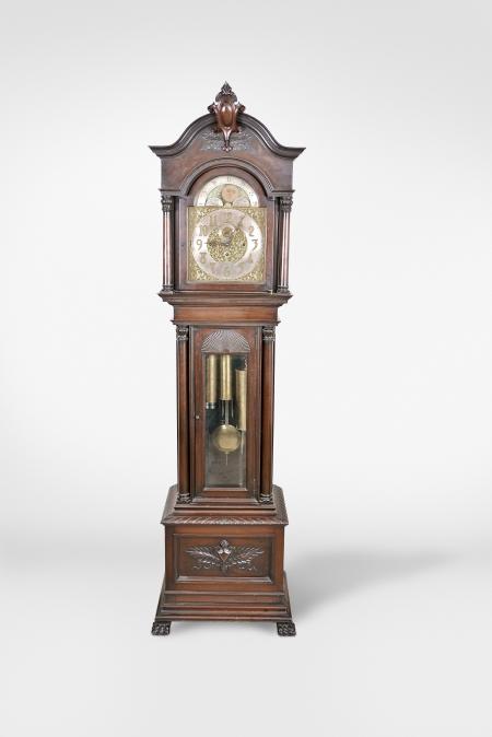 Herschede Hall Clock Co., Cincinnati, Ohio, hall clock, 8 day, time, strike and chime on five tubular bells, three brass weight driven movement in a mahogany case with arched top with central carved cartouche and applied carvings, full columns with carved capitals flanking hood door over trunk door with beveled glass and carved fan top flanked by full columns with carved capitals on base with large applied carving resting on paw feet. The brass dial has silvered chapter ring, subsidiary seconds, strike / silent and chime / silent discs, engraved brass spandrels and dial center, applied brass numerals and moon phase indicator.