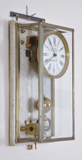 Manufacture des Ateliers Brillié Frerès, Paris, France, for J. Auricoste, Paris, "Electrique Brillié" wall clock, battery powered movement with center seconds, the heavy ball pendulum swinging through the center of the stationary electromagnet, glazed case mounted to a white marble backboard, roman / arabic white enamel dial with blackened steel Breguet hands.