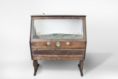 Popular Games Inc., Minneapolis, Minn., "Hoot-Mon" golf nickel arcade / skill game, made in three cabinet versions, A, B, C, golfing action figure wearing red sweater playing three holes of a par five course with painted scenery, two levers to control angle and swing and slot to accept nickel, all contained in a walnut and glass case