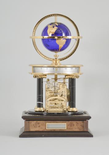 Hermle & Sohn, Germany, for the Franklin Mint, "Royal Geographical Society Millennium Clock", 8 day, time and rotating planets, spring driven movement with annular time display on a molded wood base with four black stone columns supporting a polished brass frame, gilt blue glass earth sphere and white polished stone orbiting moon, all under a glass dome.