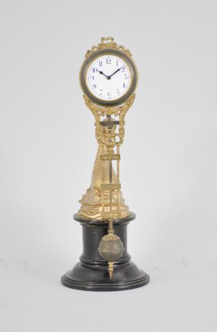 Gebrüder Junghans, Schramberg, Germany, dolphin swinging mystery clock, 8 day, time only spring driven brass movement with compound pendulum, gilt cast case, arabic numeral white enamel dial, and blued steel hands, all held aloft by the tail of a gilt cast spelter dolphin statuette on a turned ebonized wood stand.