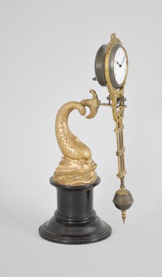 Gebrüder Junghans, Schramberg, Germany, dolphin swinging mystery clock, 8 day, time only spring driven brass movement with compound pendulum, gilt cast case, arabic numeral white enamel dial, and blued steel hands, all held aloft by the tail of a gilt cast spelter dolphin statuette on a turned ebonized wood stand.