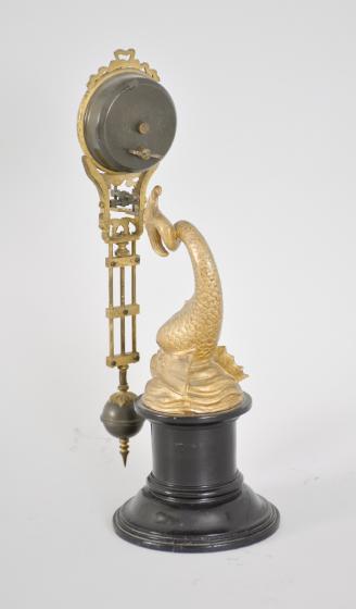Gebrüder Junghans, Schramberg, Germany, dolphin swinging mystery clock, 8 day, time only spring driven brass movement with compound pendulum, gilt cast case, arabic numeral white enamel dial, and blued steel hands, all held aloft by the tail of a gilt cast spelter dolphin statuette on a turned ebonized wood stand.