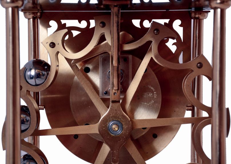 Dove Bazely Ltd., Cheltenham, England, Perpetuum clock, polished brass portico style case with mahogany base, Roman numeral silvered dial, 8 days, timepiece movement powered by a spring, and 24 steel balls, which drop from the rail on the case top onto the "ferris wheel" attached to the winding arbor behind the movement, with paperwork, c1986