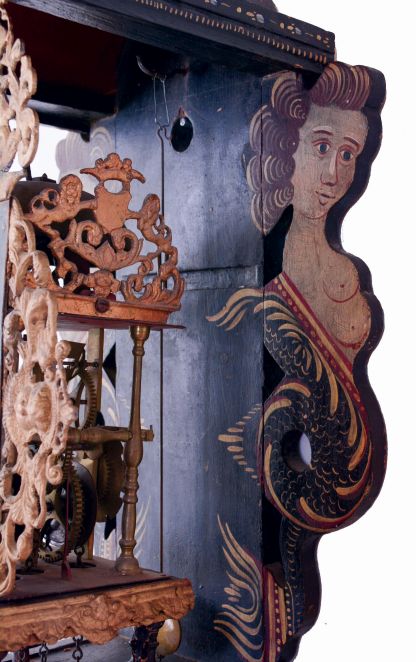Frisian stoelklok, polychrome painted shelf with mermaids and painted floral decoration, lead ornaments with gilding and with painted swan, Roman numeral painted, arcaded dial with a disturbing pair of reclining figures, urn with flowers, and central vignette with landscape and a building, pierced brass hands, typical baluster turned brass four pillar, time and strike movement with alarm, bell hammer arbor of brass and with matching baluster turnings, large brass pear shaped weight, late 18th- early 19th century