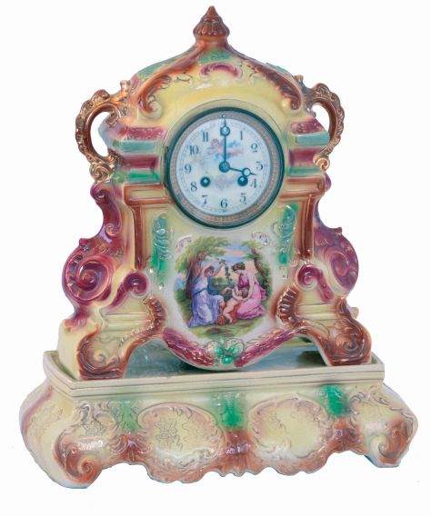 England, Strasburg Ware clock, with French movement, colorful earthenware case, enamel scene with figures in a landscape below the dial, Arabic numeral white enamel dial with putto and floral festoon, the case resting on its original Strasburg Ware base, 8 days, time and strike movement, c1920