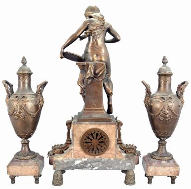 Irving Miller & Co., France, three-piece figural mantel clock with garniture, red and grey marble base on cast bell-shaped feet supporting clock with polychrome enamel dial, flanked by acanthus ornaments and surmounted by a cast spelter female figure depicting youth titled "Jeunesse". The movement is an 8 day spring driven time and strike pendule de Paris. Matching marble and cast metal vases with lids.