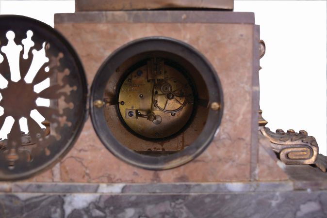 Irving Miller & Co., France, three-piece figural mantel clock with garniture, red and grey marble base on cast bell-shaped feet supporting clock with polychrome enamel dial, flanked by acanthus ornaments and surmounted by a cast spelter female figure depicting youth titled "Jeunesse". The movement is an 8 day spring driven time and strike pendule de Paris. Matching marble and cast metal vases with lids.