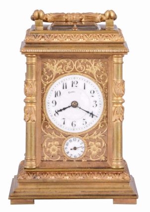 France, for Tiffany & Co., a Pillars style, petit sonnerie striking carriage clock with repeat, the glazed, gilt case with bright and matte surfaces, the base and cornice with cavetto and egg and dart moldings, the corners with acanthus decorated columns, and carrying handle also with foliate ornament, Arabic numeral white enamel dial with fretted, matte gilt foliate mask against a bright gilt background, blued steel distaff hands, 8 day time, strike, and alarm movement with lever platform, sounding petit sonnerie quarters in passing, with grand sonnerie repeating on demand, the base with strike/ silent lever