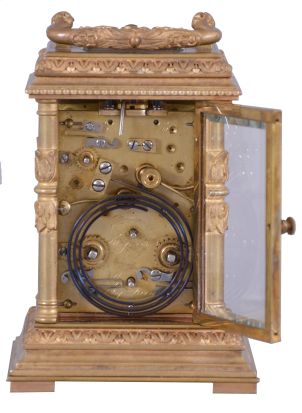 France, for Tiffany & Co., a Pillars style, petit sonnerie striking carriage clock with repeat, the glazed, gilt case with bright and matte surfaces, the base and cornice with cavetto and egg and dart moldings, the corners with acanthus decorated columns, and carrying handle also with foliate ornament, Arabic numeral white enamel dial with fretted, matte gilt foliate mask against a bright gilt background, blued steel distaff hands, 8 day time, strike, and alarm movement with lever platform, sounding petit sonnerie quarters in passing, with grand sonnerie repeating on demand, the base with strike/ silent lever