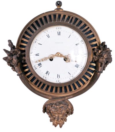 Gilt Brass Cartel Wall Clock with 7.5 inch porcelain roman numeral dial marked "Tiffany" and "France", pierced gilt hands all set in a cast brass fluted case with overflowing cornucopias of flowers and fruit at the sides and a mythological god of plenty mask at the bottom, eight-day French spring powered movement with lever platform escapement and bell strike.