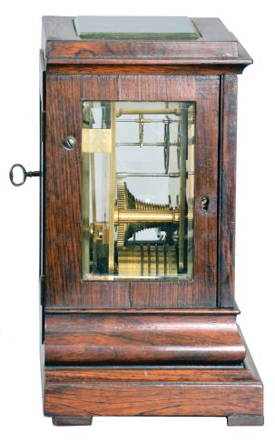 England, a miniature rosewood bracket form fusee timepiece, the glazed, architectural case with footed, molded base supporting a bombe surface the upper, rectilinear portion with cavetto cornice molding, Roman numeral silvered dial with blued spade and whip hands, the door with matching, silvered liner, 8 day, brass timepiece movement with recoil escapement, and brass pendulum with tie down for transport