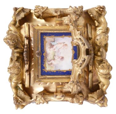 Attributed to Drocourt, Paris, a rare and extremely decorative giant carriage clock in the rococo style, the gilt case replete with scrolls, foliate ornament, and putti, and set with eight gilt and polychrome enamel porcelain plaques featuring garden scenes and frolicking amorini, each on a deep blue field with gilt, foliate border, the Roman numeral dial with blued steel hands, case back with sliding glass panel to allow access for winding and setting, 8 day time, strike, and alarm movement with lever platform, repeating the last hour on demand, gong base marked "A.D." within an oval, serial #29268