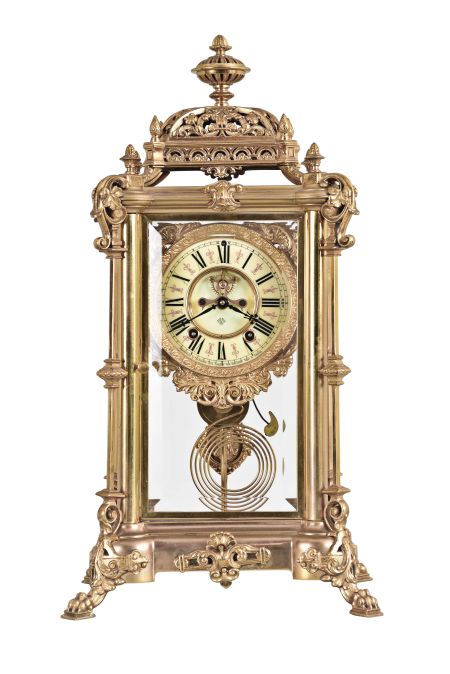 Ansonia Clock Co., New York, "Excelsior" crystal regulator, 8 day, time and strike, spring driven movement with visible Brocot escapement in a gilt finished brass case on claw feet, cream porcelain dial with Roman numerals and red interstitial decorations, cast pendulum with female face, strikes on cathedral gong.