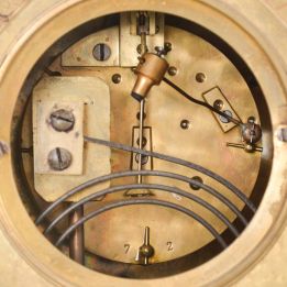 France, Mantel Clock with porcelain roman numeral dial and decorative cast center, blued-steel hands, complicated classical-styled cast brass case with urn finial at the top flanked by griffins, a female goddess of the sun life mask surmounting the dial, four fluted columns supporting the whole and a leaf and scroll base with cross hatching and four scroll-leafed feet, round brass French eight day movement with rack hour striking on a gong and pendulum.