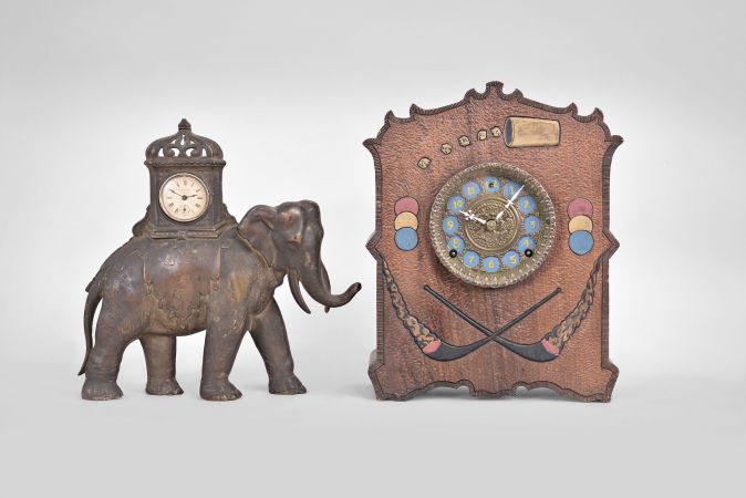 Clocks- 2 (Two): (1) Golden Novelty Mfg. Co., Chicago, elephant novelty clock, 30 hour, time only, spring driven balance wheel movement in a cast iron case shaped like an elephant, c1895; (2) Wm. L. Gilbert Clock Co., Winsted, Conn., "Cosey Corner, Pattern R" cabinet clock, 8 day, time and strike, spring driven movement in burnt wood case with dice, cards, poker chips, and domino designs, c1906.