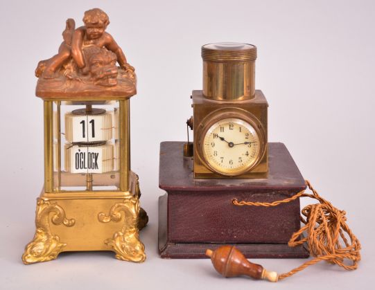 Clocks- 2 (Two): (1) Lenzkirch AG, Lenzkirch, Germany, digital flip card clock, spring driven balance wheel movement in a glazed case with dolphin-form feet, surmounted by a child wresting a sea creature, c1900; (2) Projection clock, 30 hour, time and light projection, spring driven balance wheel movement in a brass case with battery compartment in the base and corded push-button switch, c1920.