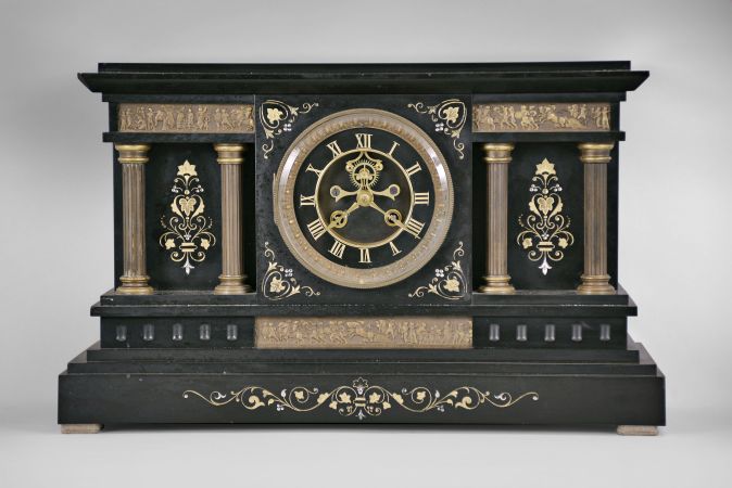 France, mantel clock, 8 day, time and strike, spring driven pendule de Paris movement with visible Brocot escapement in a black slate case with incised floral designs, gilt metal columns, and three classically inspired low-relief friezes depicting a crowd, chariot, soldiers, and an elephant, black slate dial with incised gold Roman numerals and gilt hands.