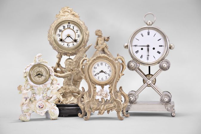 Clocks- 4 (Four): (1) Waterbury Clock Co., Waterbury, Conn., mantel clock, 8 day, time and strike, spring driven movement in a cast metal case featuring a putto holding the clock aloft, cream porcelain dial, 1915; (2) Austria, mantel clock, 2 day, time and strike, spring driven movement in a silver plate-over-copper case with white enamel dial, c1840; (3) Waterbury Clock Co., Waterbury, Conn., novelty clock, 30 hour, time only movement with thread suspension in a cast metal case with painted ceramic panel and topped by putto figure, c1905; (4) Germany, novelty clock, 30 hour, time only, spring driven movement in a porcelain case with putti figures, c1920.