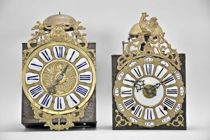 Clocks- 2 (Two) Comtoise with Cartouche Numerals: (1) France, bronze-front Comtoise clock, 8 day, time and strike with alarm, weight driven movement with verge escapement, thread suspension with rear-hanging pendulum in an iron post and plate frame, cast brass dial with royal symbols including a crown and profile of Louis XV, white enamel cartouche numerals with blue lettering, topped by cast fronton featuring fleur de lis and the backward facing Gallic rooster, applied lower casting, and single iron hand, mid 18th Century. (2) France, bronze-front Comtoise clock, 8 day, time and strike with alarm, weight driven movement with verge escapement, thread suspension with rear-hanging pendulum in a posted frame, 25 white enamel panels inset within cast brass dial, two iron hands, pieced brass spandrels, and topped by cast fronton with backward facing Gallic rooster, mid 18th Century.